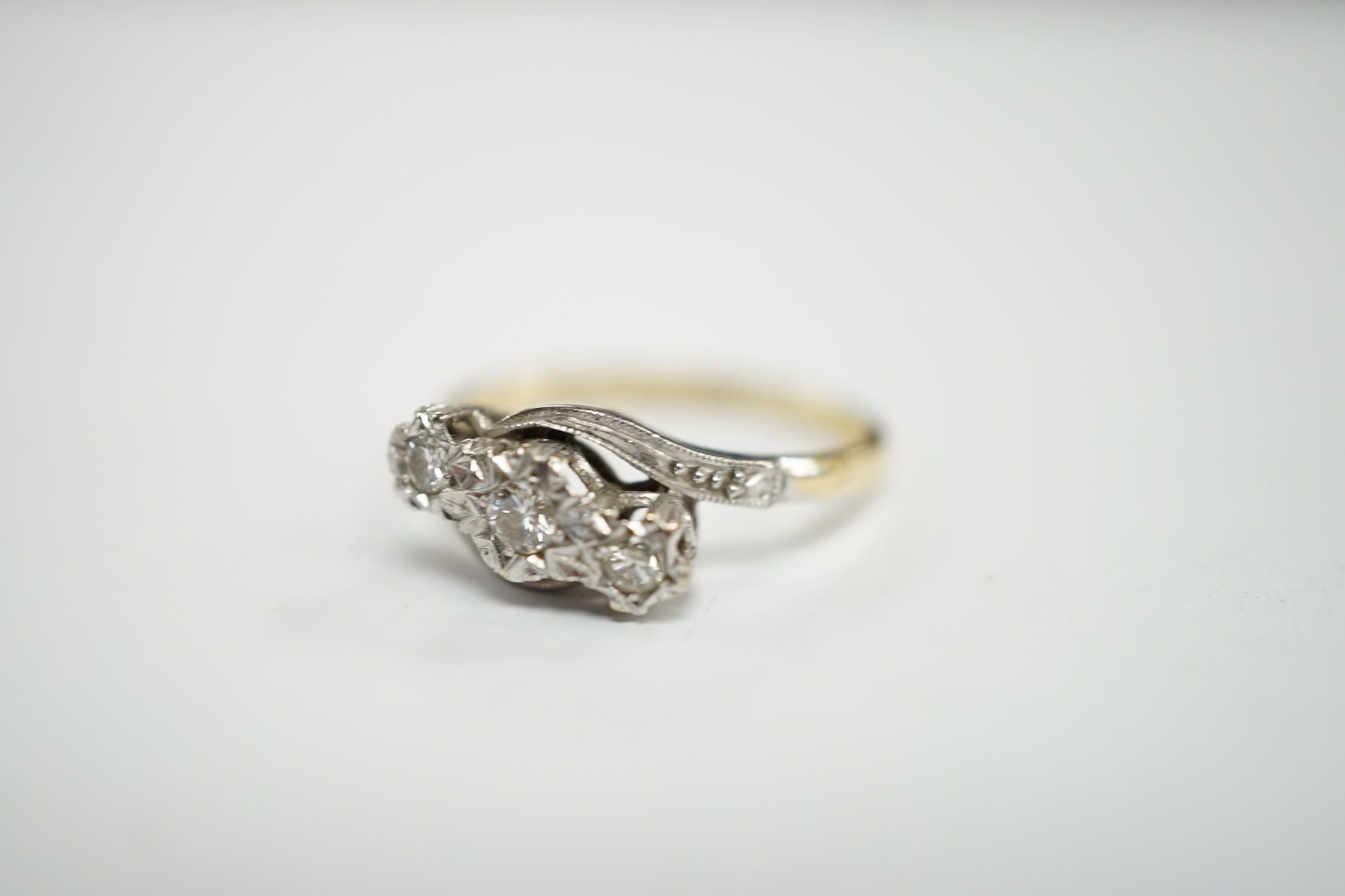 A mid to late 20th century 18ct gold and illusion set three stone diamond crossover ring, size N, gross weight 3.3 grams.